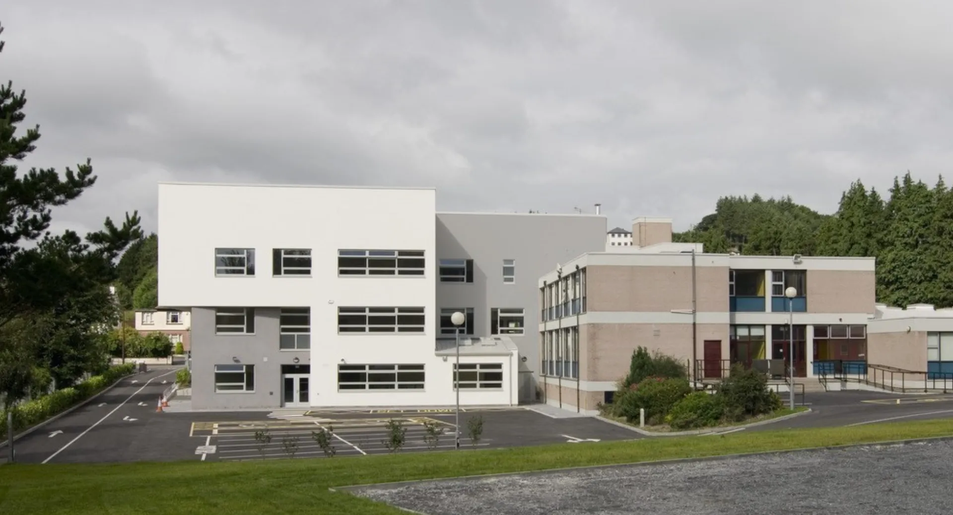 L'edificio moderno a più piani del Castleblayney College è circondato da prati e alberi sotto un cielo nuvoloso.