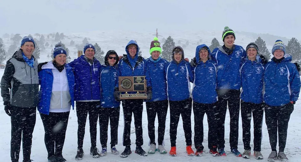 Un gruppo di studenti e studentesse della Sioux Falls Christian School posa in divise da sport invernali blu e grigie davanti a un paesaggio montano innevato.