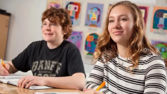 Dos estudiantes de Calmar Secondary School se sientan en el aula frente a una pared con obras de arte.