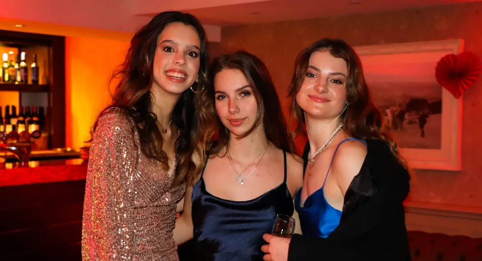 Tre studentesse della RGS Surrey Hills posano insieme in un ristorante con luci colorate sullo sfondo.