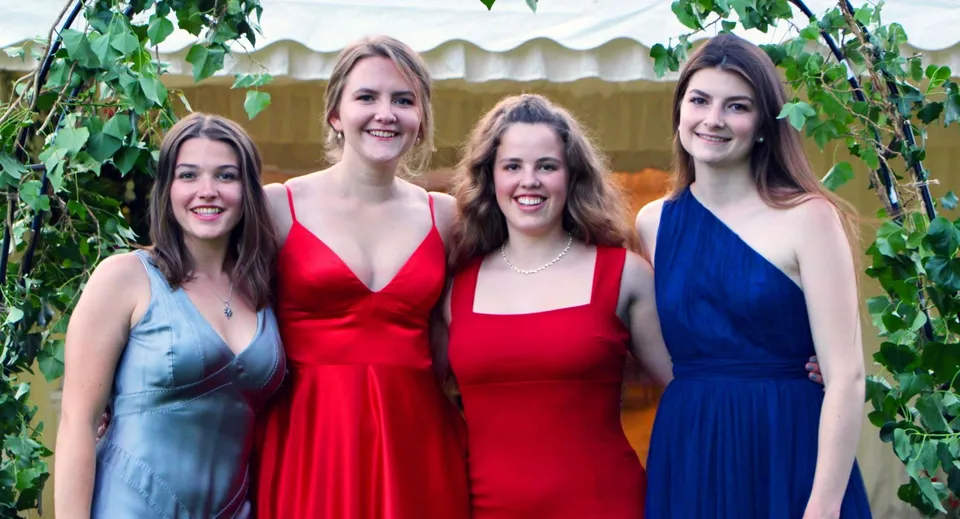 Quattro giovani donne in abiti colorati posano davanti a uno sfondo verde nel campus della Headington School.