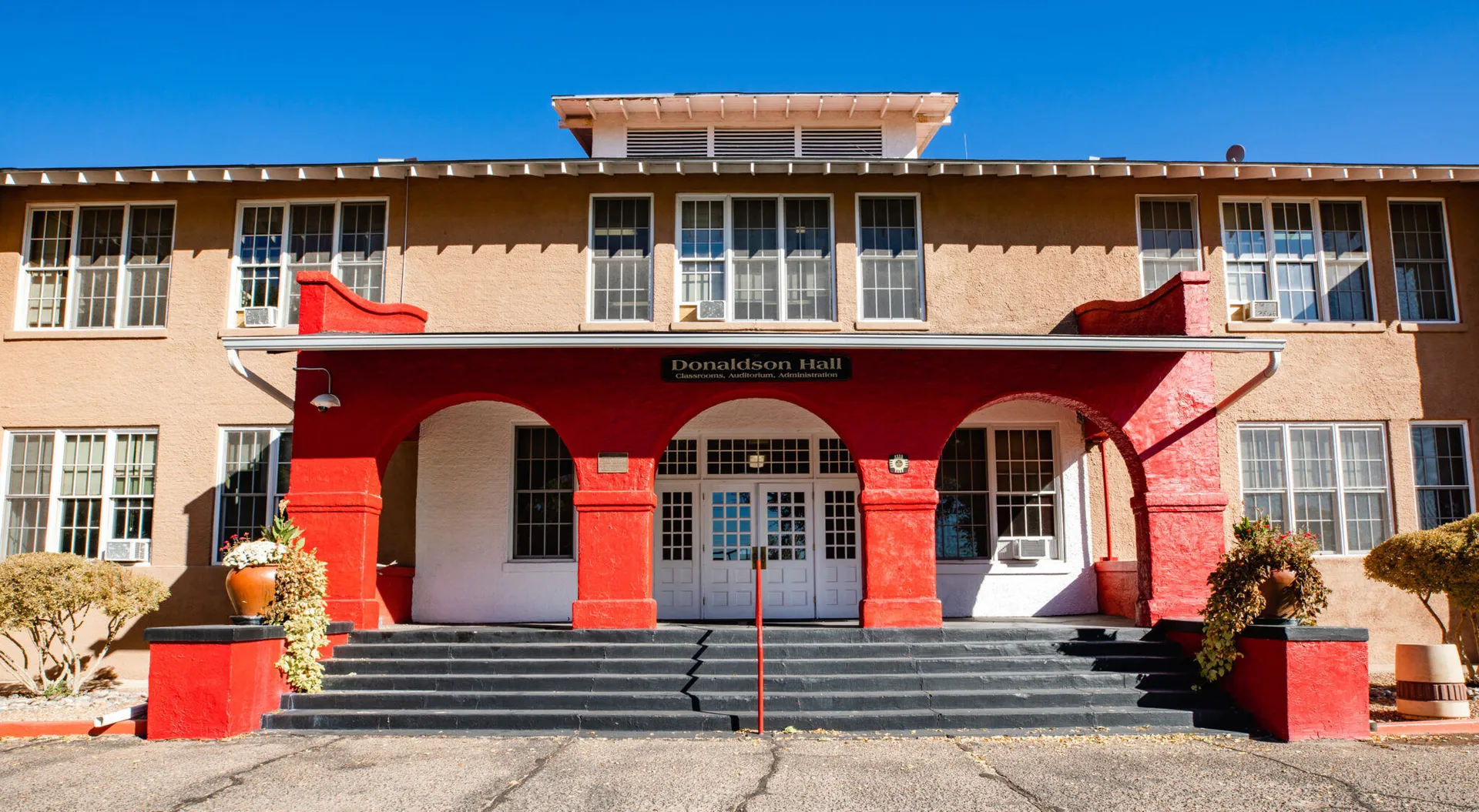 L'edificio a due piani con ingresso rosso della Menaul School sotto un cielo blu terso.