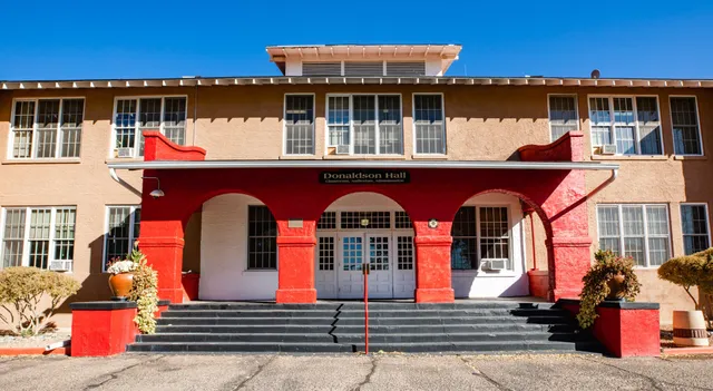 L'edificio a due piani con ingresso rosso della Menaul School sotto un cielo blu terso.