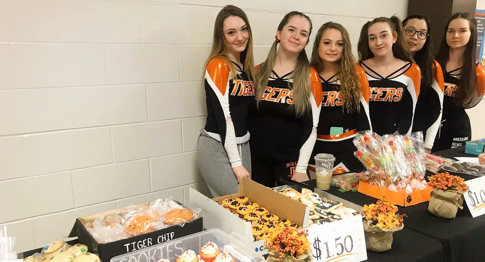 Un gruppo di studentesse della McNally High School è insieme davanti a una parete e vende vari oggetti.