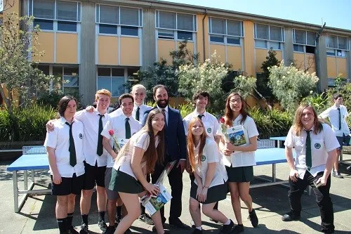 Un grupo de estudiantes está frente a un edificio con grandes ventanas en el campus de The Forest High School.