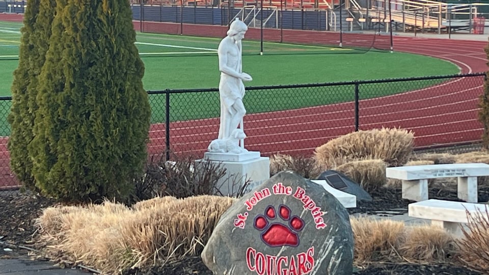 Gli impianti sportivi della St. John the Baptist High School con pista di atletica, una statua e un masso con il logo dei Cougars.