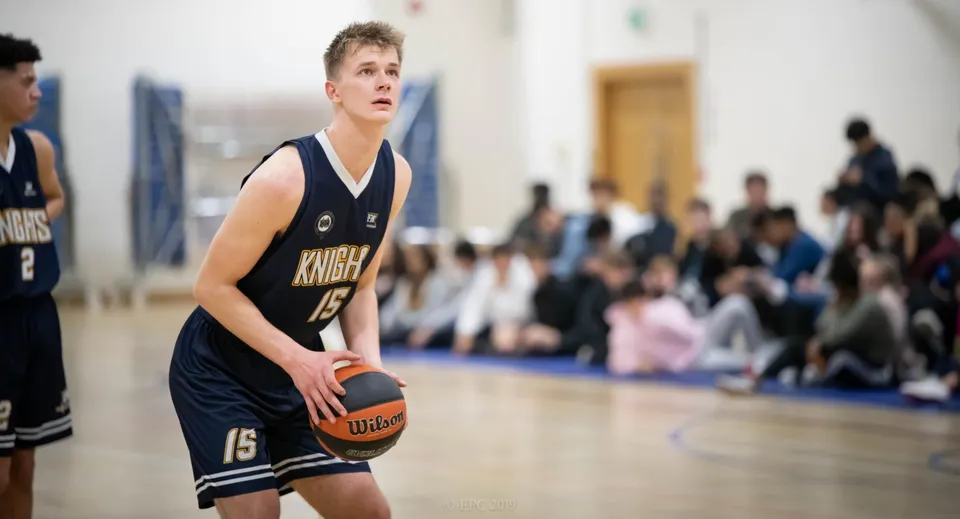 Un giocatore di basket del Queen Ethelburga’s Collegiate è sul campo da basket davanti a una tribuna per lo spettacolo.