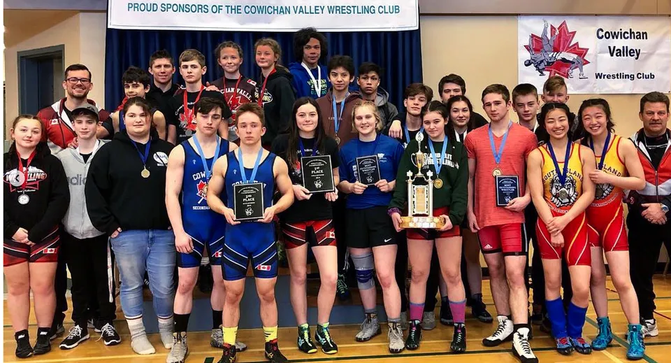 Un gruppo di giovani lottatrici della Chemainus Secondary School si trova con dei trofei davanti a uno striscione del Cowichan Valley Wrestling Club.