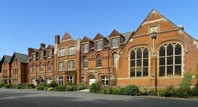 Una serie di edifici in mattoni decorati con tetti a punta nel campus del Kent College sotto un cielo limpido.