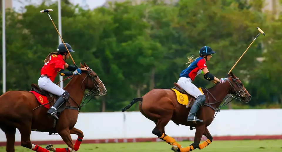 Due giocatrici di polo a cavallo sul campo della Branksome Hall davanti a un paesaggio verde.