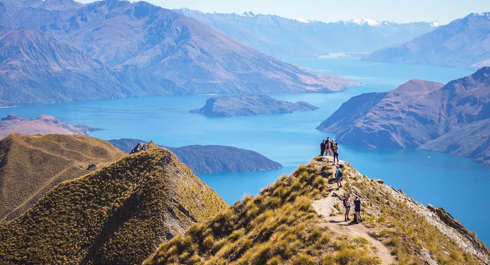 Due studenti del Manawatu College si trovano durante un'escursione su uno sperone roccioso con vista su un lago di montagna turchese.