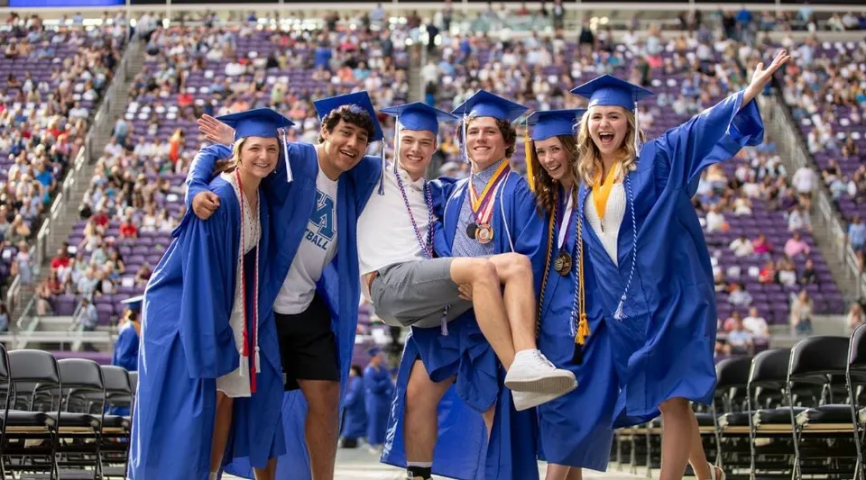 Un gruppo di diplomati delle Minnetonka Public Schools in toga blu insieme in un ambiente simile a uno stadio.