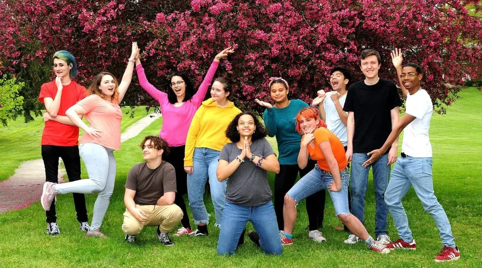 Un gruppo di studenti della Oakwood Friends School si trova in un campo davanti ad alberi con fiori rosa.