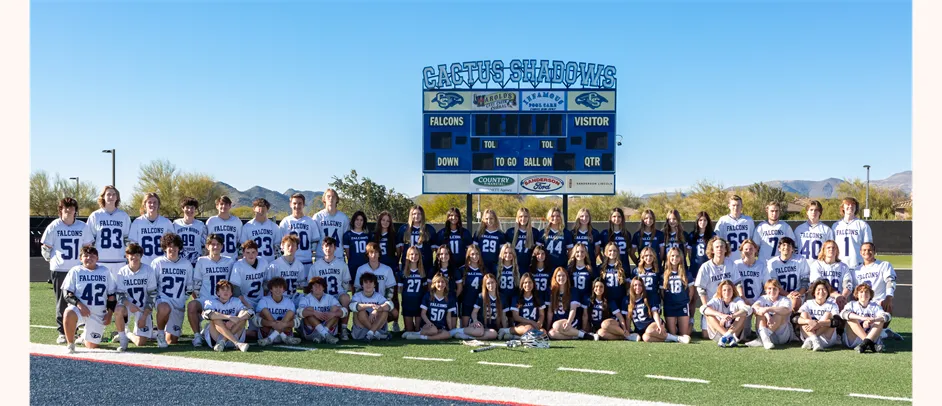 Jugadoras y jugadores de fútbol de Cactus Shadows High School están en el campo frente a un marcador con montañas al fondo.