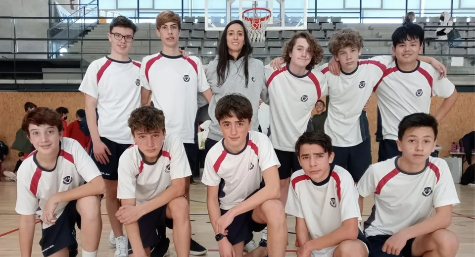 Un gruppo di studenti della SEK International School Catalunya posa in un palazzetto dello sport con un canestro da basket sullo sfondo.