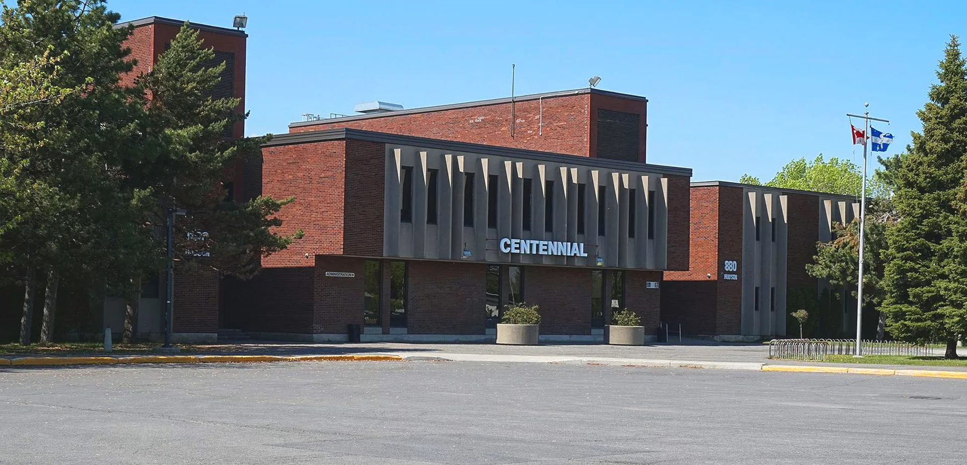 Il grande edificio in mattoni della Centennial Regional High School è circondato da alberi e si trova davanti a un'area pavimentata.