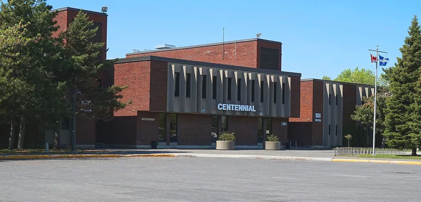 Il grande edificio in mattoni della Centennial Regional High School è circondato da alberi e si trova davanti a un'area pavimentata.