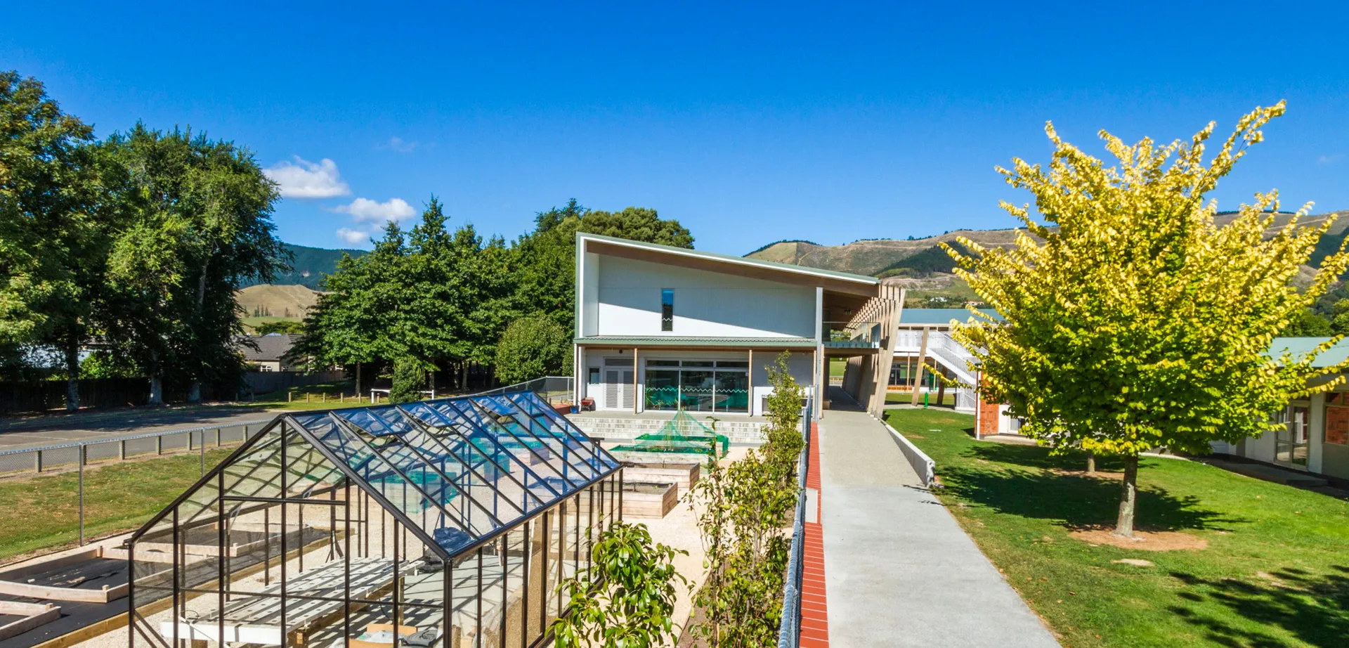 L'edificio moderno e a vetrate del Waimea College è circondato da aree verdi e da un viale lastricato, con le montagne sullo sfondo.