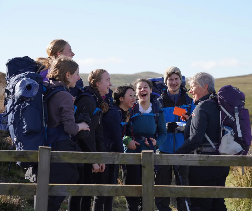 Un gruppo di studenti della Edinburgh Steiner School si trova su una piattaforma in legno all'aperto, con vista su un paesaggio collinare e un cielo terso.