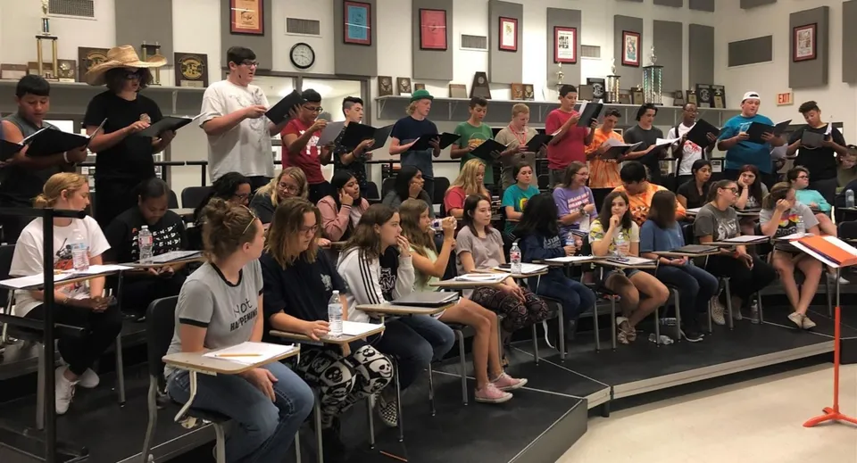 Studenti e studentesse della Walpole High School provano con cartelline di spartiti in un'aula di musica.