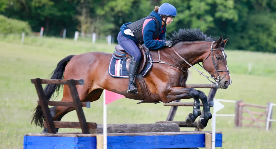 Un cavaliere con casco blu salta un ostacolo con un cavallo marrone nella proprietà del Pangbourne College.