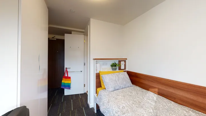 Camera singola di Parry Hall con letto, testiera in legno e armadio bianco accanto alla porta