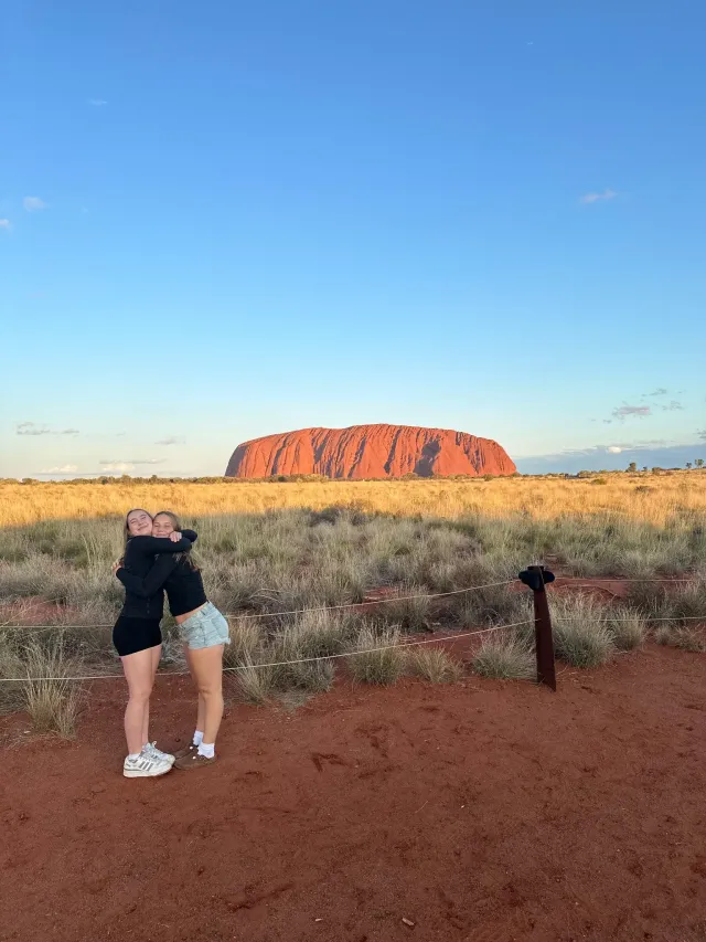 Due amiche si abbracciano sorridendo davanti a Uluru al tramonto in Australia