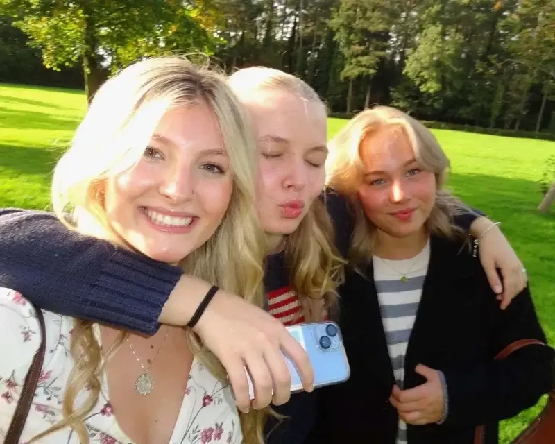 Selfie de tres chicas rubias abrazadas en un parque con césped y árboles