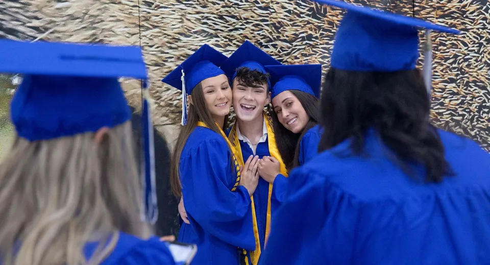 I diplomati della Canterbury High School festeggiano il loro diploma in toga e tocco blu davanti a uno sfondo di alberi.