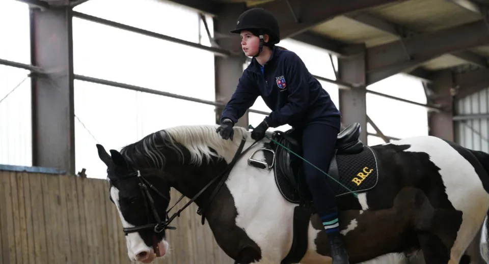 Una studentessa in tenuta da equitazione è seduta su un grande cavallo scuro nel maneggio della TASIS The American International School in England.