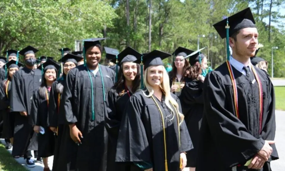 Un gruppo di diplomati del New Brunswick Community College si trova in abito accademico in un'area esterna alberata.