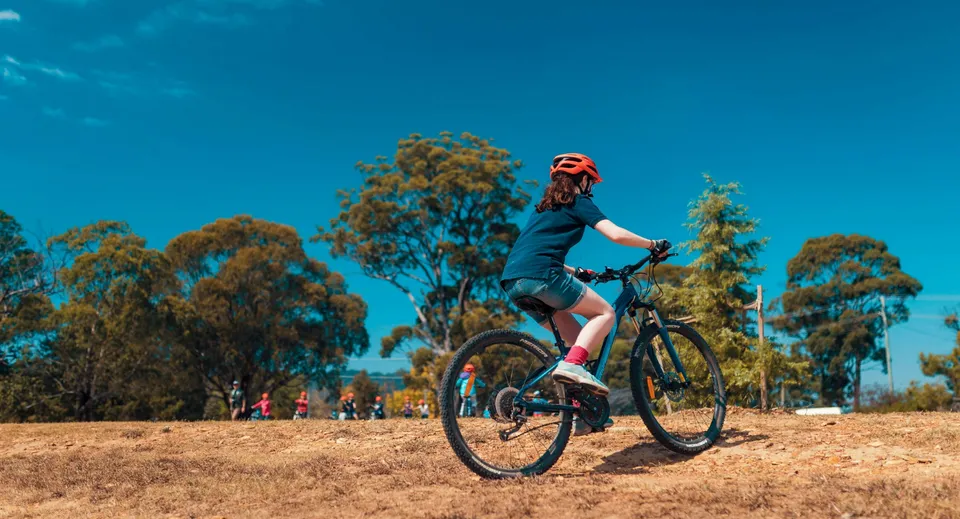 Una studentessa del Meridan State College guida una mountain bike su un sentiero nel bosco sotto un cielo blu.
