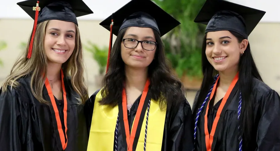 Tre diplomande in toga stanno insieme nel campus della RGS Surrey Hills e sorridono.