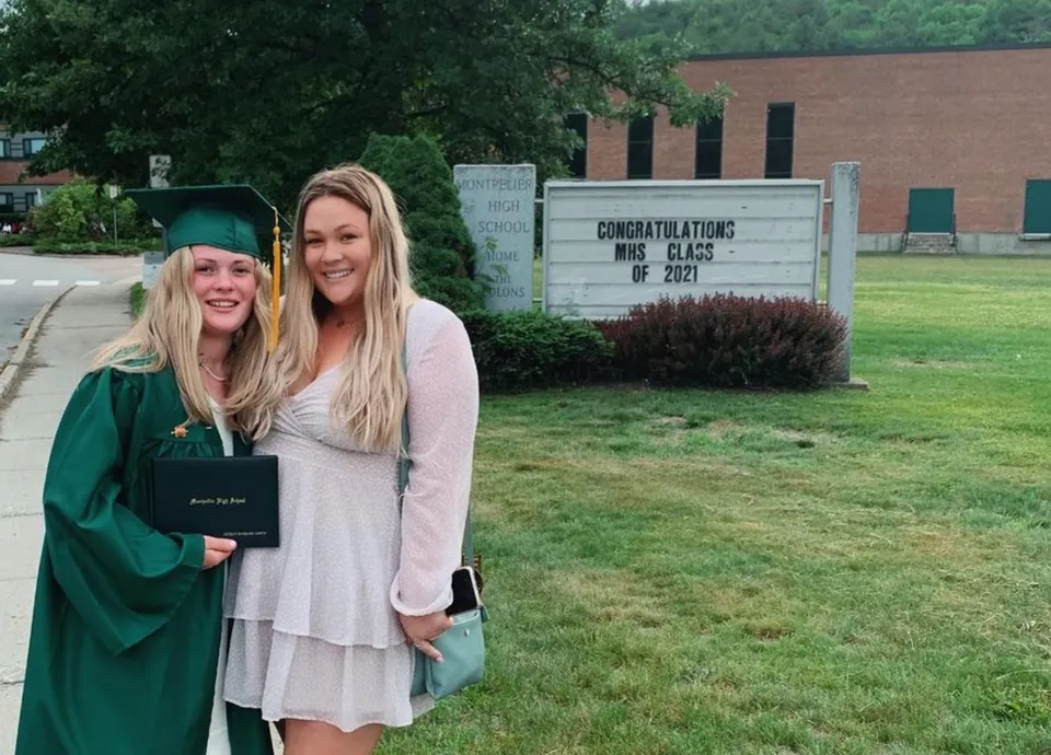Due studentesse in toga da laurea si trovano davanti a un cartello con gli auguri per la classe del 2022 nel campus della Montpelier High School.
