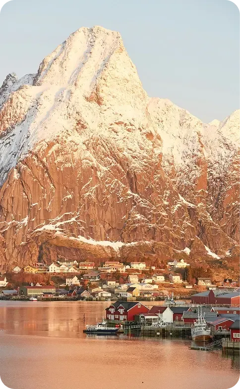 Villaggio di pescatori con cabine rosse ai piedi di una montagna innevata su un fiordo norvegese