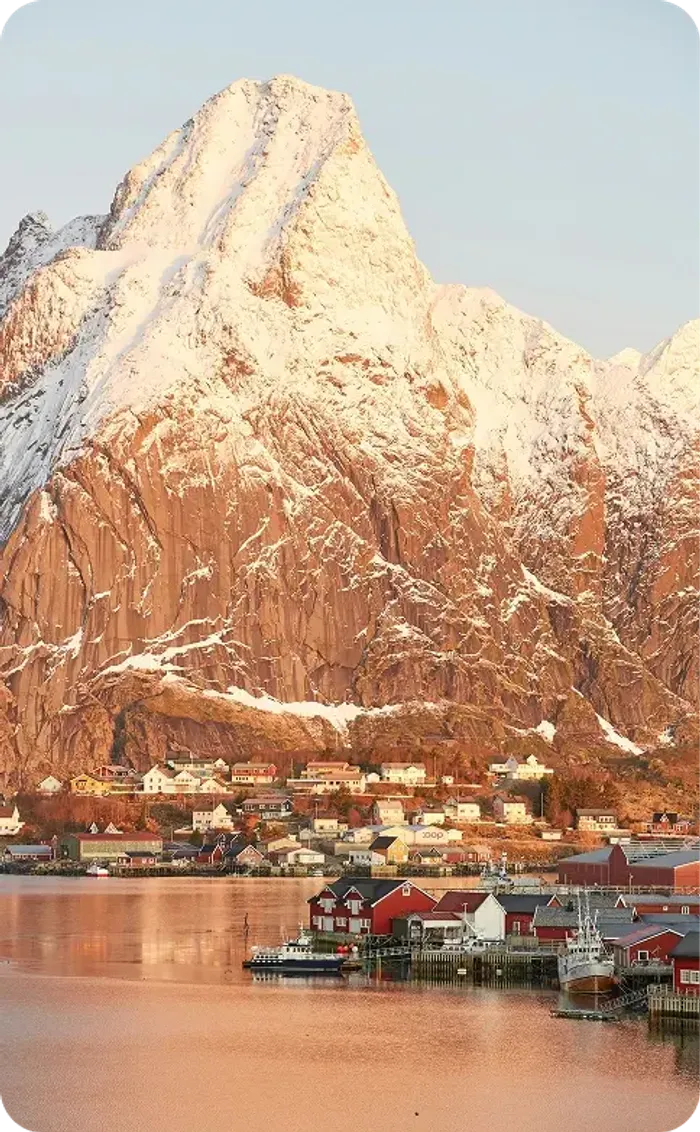 Villaggio di pescatori con cabine rosse ai piedi di una montagna innevata su un fiordo norvegese