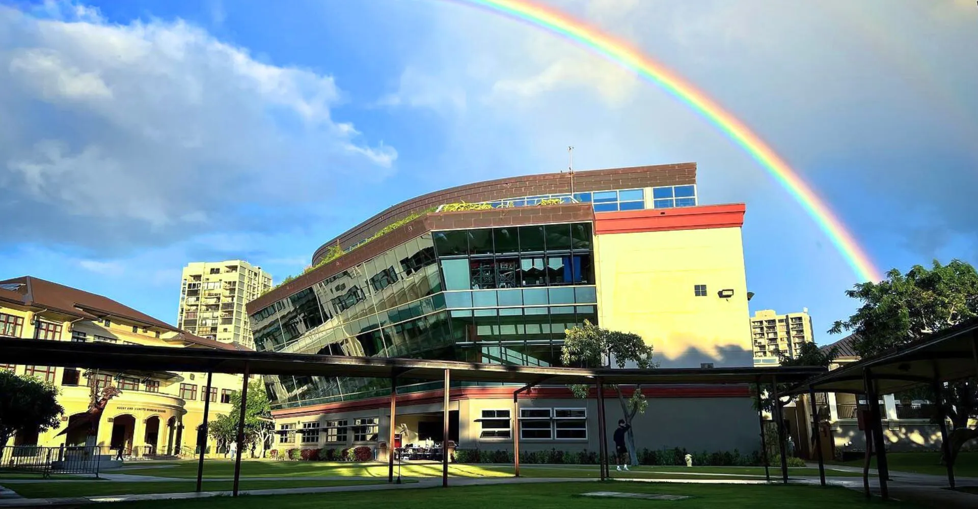 Un arcobaleno colorato si staglia sopra l'edificio moderno della Iolani School con un cortile in primo piano.