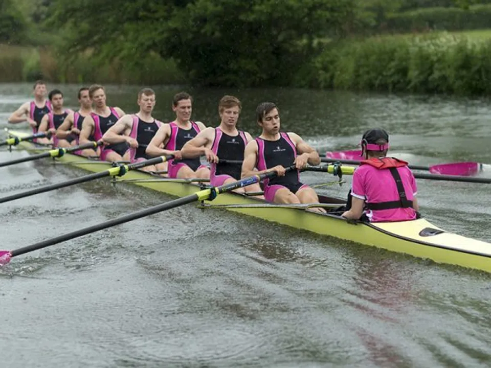 La squadra di canottaggio della Abingdon School si allena su un fiume circondato da una verde vegetazione.