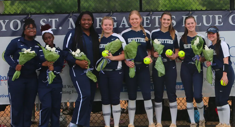 Un gruppo di giocatrici di softball in uniforme davanti a una recinzione con uno striscione della St. Margaret's School.