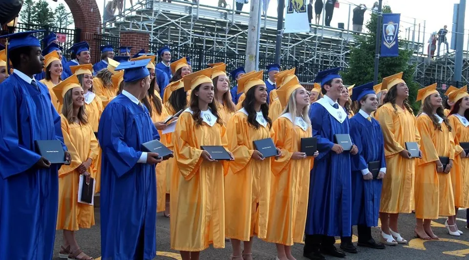 Un gruppo di diplomati della Marian Catholic High School in toga blu e gialla davanti a un ponteggio e ad alcuni edifici.