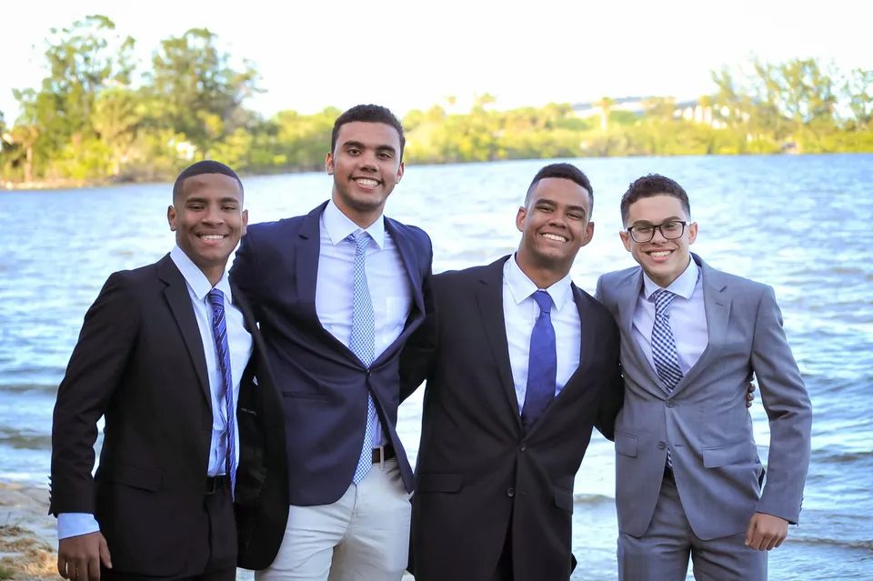 Quattro uomini in abito formale insieme davanti a uno specchio d'acqua nel campus della Florida Preparatory Academy.