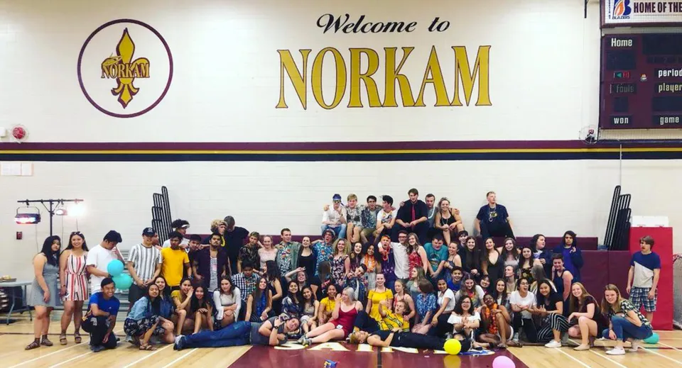 Un gruppo di studenti e studentesse si trova davanti al cartello di benvenuto della NorKam Secondary School.