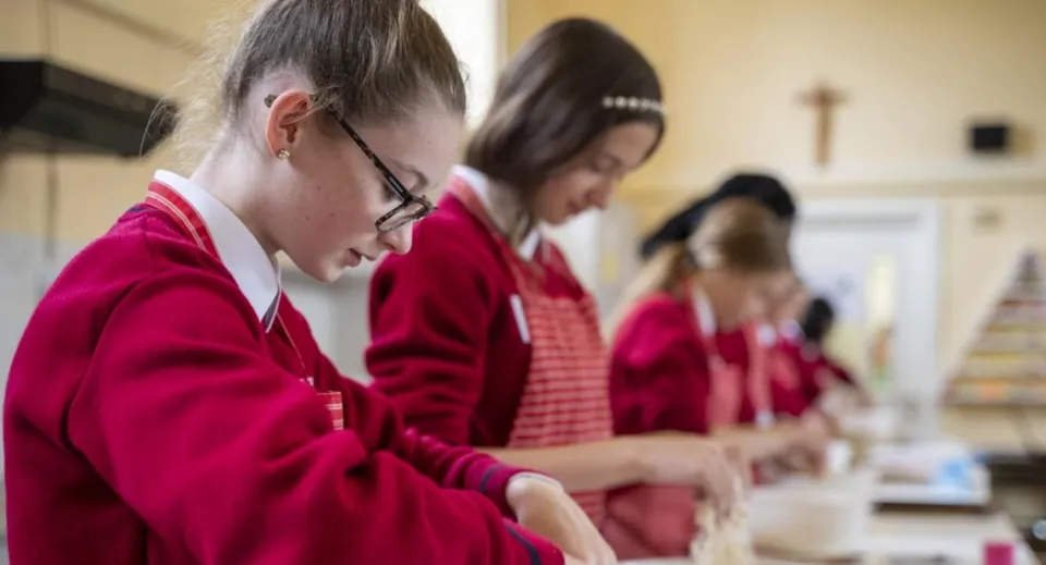 Studenti del St. Dominic’s College indossano toghe rosse e sono impegnati in una discussione di gruppo.