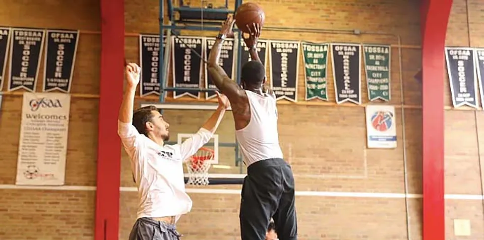 Due studenti del George Harvey Collegiate Institute giocano a basket in una palestra con striscioni sportivi sullo sfondo.