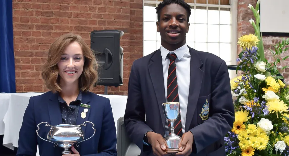 Due persone in abiti formali tengono dei trofei durante una premiazione nel campus della Pocklington School.