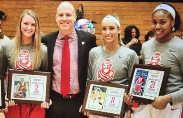 Un hombre con traje junto a tres jugadoras de baloncesto que sostienen cuadros conmemorativos
