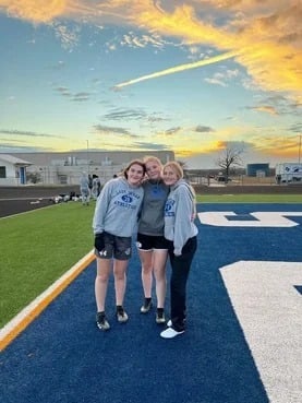 Tres estudiantes abrazadas en el campo deportivo del colegio al atardecer