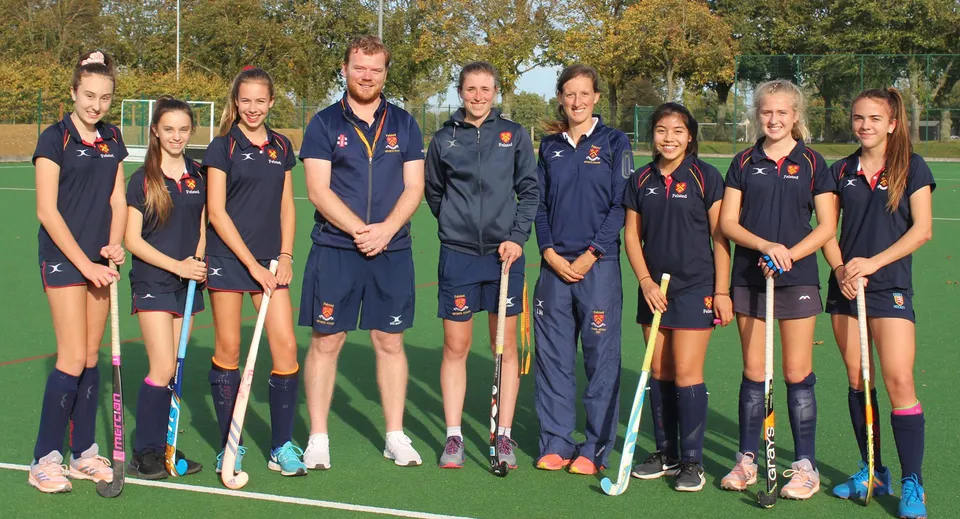 Un gruppo di giovani giocatori e giocatrici di hockey si trova insieme sul campo sportivo della Felsted School.