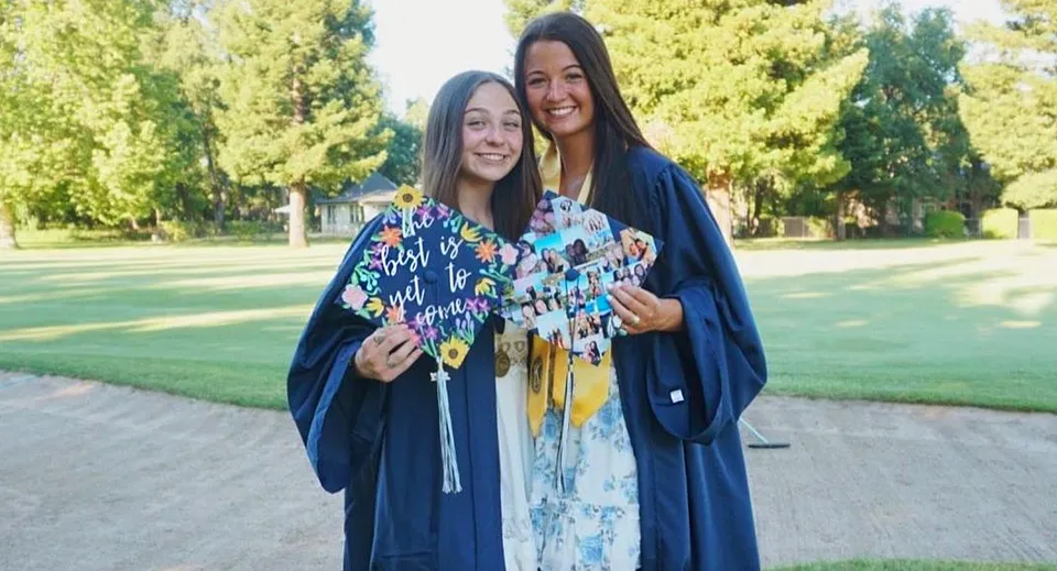 Due studentesse in abito da cerimonia di diploma colorato sono nel parco del Chico Unified School District e sorridono insieme.