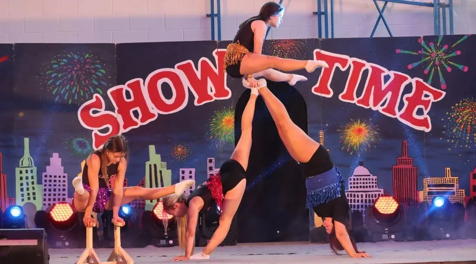 Un gruppo di performer si trova sul palco con la scritta Show Time sullo sfondo nel campus del Largy College.